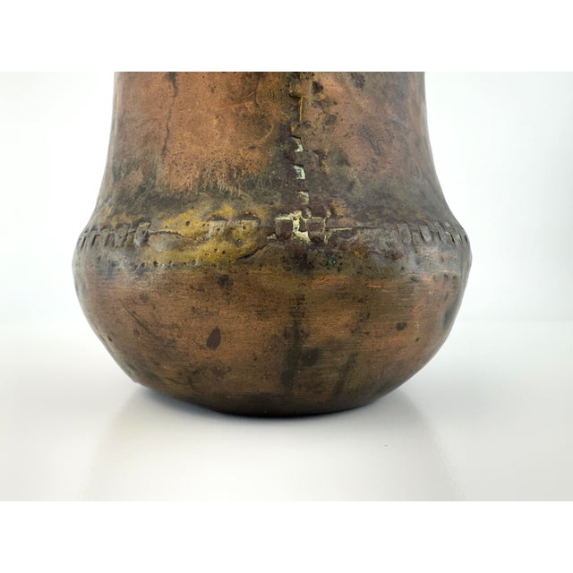Antique hand-hammered copper vessel with a substantial, rounded form and visible riveted seam detailing. The richly...