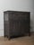 A wooden sideboard with a dark, matte surface and a straightforward paneled construction. The upper section contains a...
