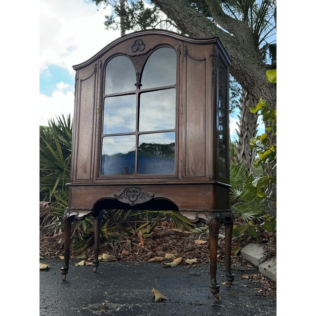 An elegant antique French Provincial display cabinet showcasing graceful lines, beautifully carved detailing, and a warm...