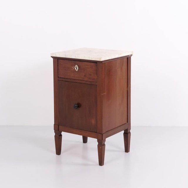 Mahogany bedside table with a marble top, one drawer, and one cupboard door. Dating from the 1930s, it offers practical...