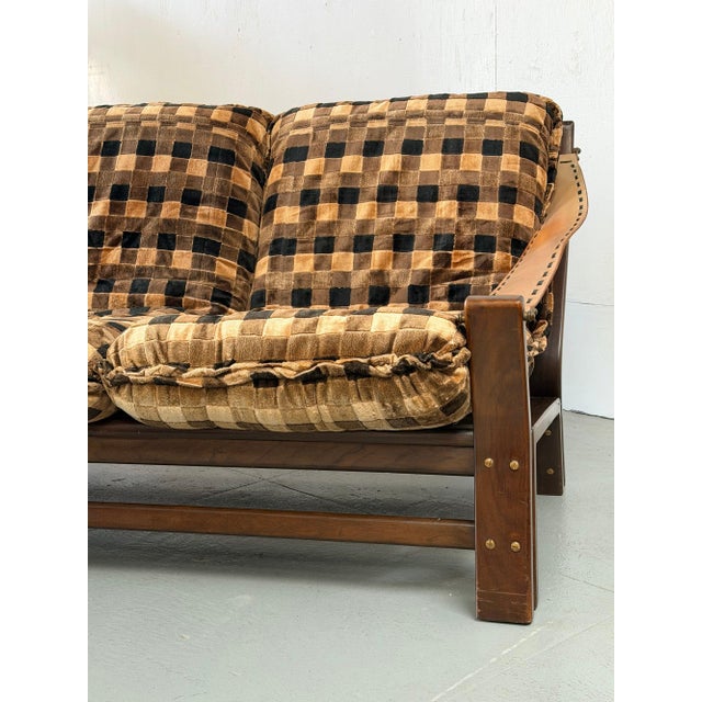 A three-seat sofa built around a sculpted solid wood frame, with leather arm straps adding a tailored, saddlery-like...