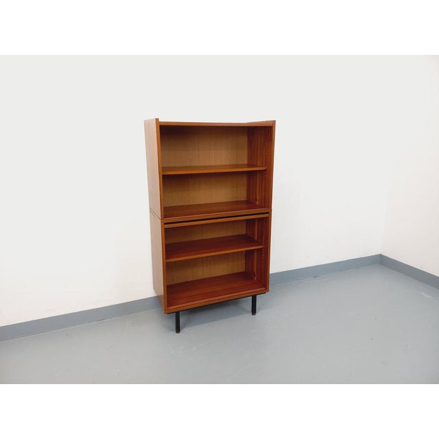 1960s modernist style bookcase in teak-style mahogany, black metal legs with brass leveling feet, four open interior...