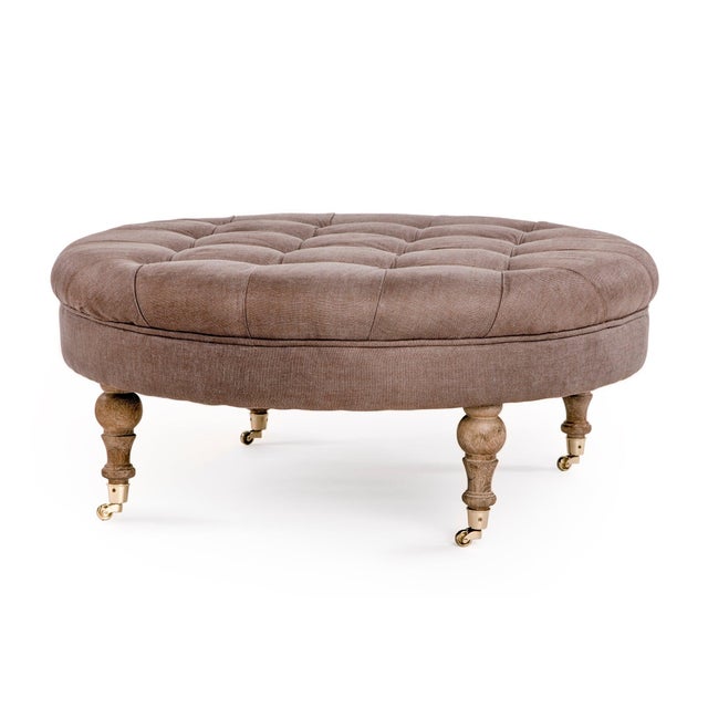 The Maison Tufted Round Ottoman from Zentique features a generous round button-tufted top on turned wood legs with brass...