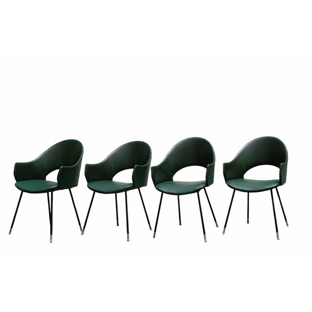 Set of 4 chairs/armchairs with round backrests, featuring four elongated, slanted iron legs with brass tips for support....