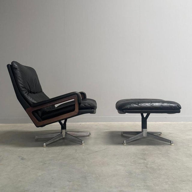 Remarks: King chair with hocker by André Vandenbeuck for Strässle, Switzerland 1960s. Black leather upholstery with steel...