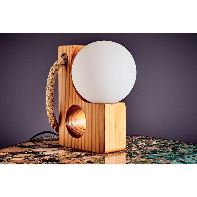 Table lamp by Temde Leuchten, featuring a sculpted pinewood block with circular cut-outs, a braided natural-fiber loop for...