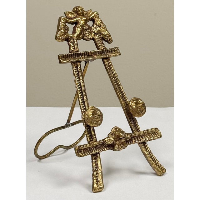 Vintage brass table easel with intricate design. Features angel figure to top with lion emblem to lower bar. Lion head...