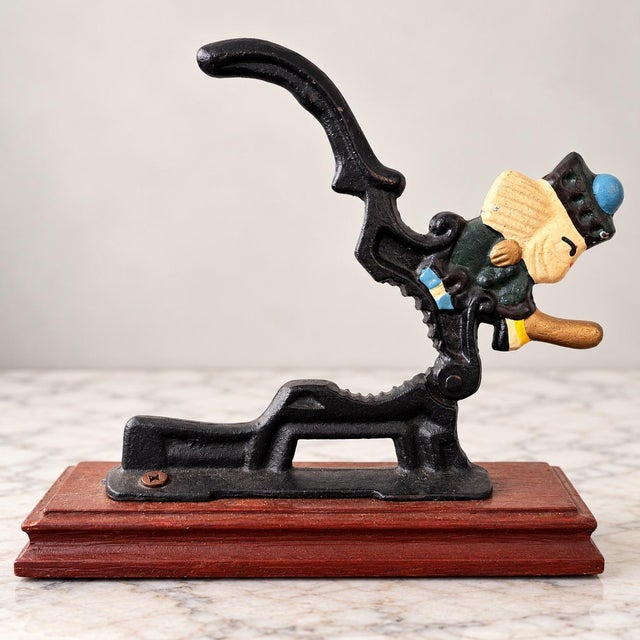 Charming vintage cast iron nutcracker featuring a beautifully detailed, hand-painted soldier figure mounted on a rich wood...