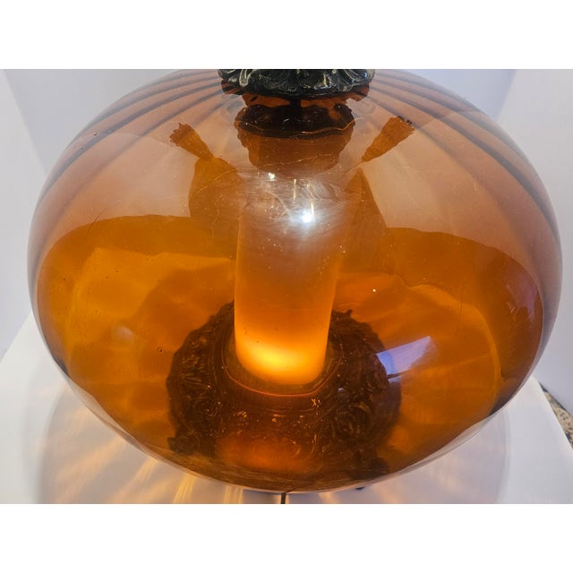 Striking oversized vintage table lamp featuring a dramatic amber smoked glass globe body with ornate antiqued metal...