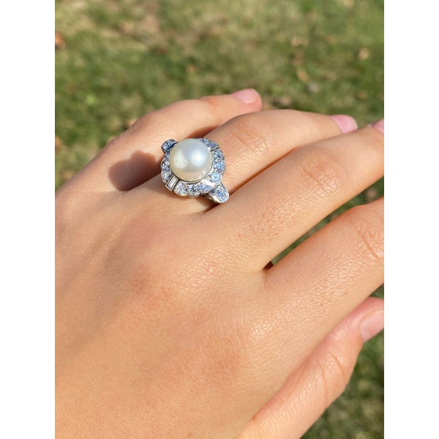 The 114th Avenue: Antique Natural Pearl and Diamond Ring in Platinum. Centered around a captivating 10.4-millimeter...