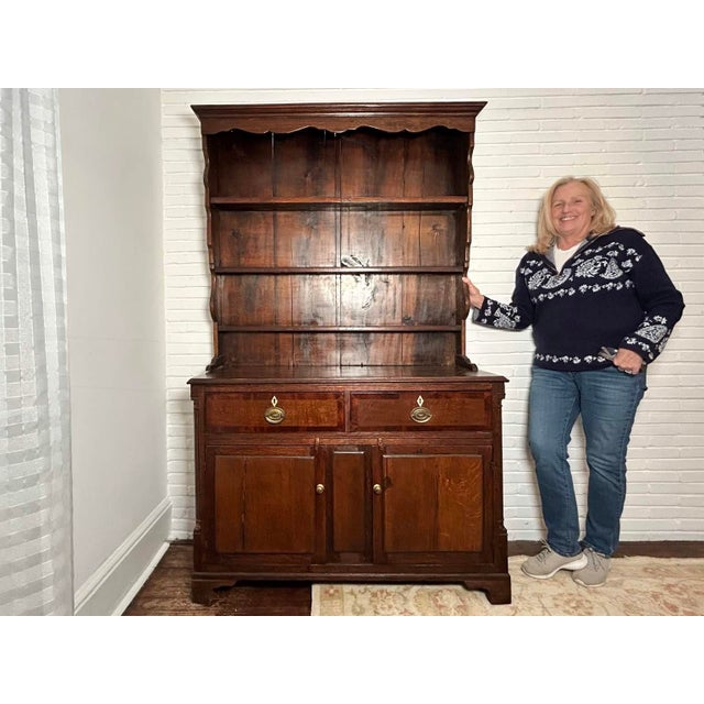 A two-piece antique English oak Welsh dresser, hutch or cupboard cabinet with a scalloped edge crown, three shelves with...