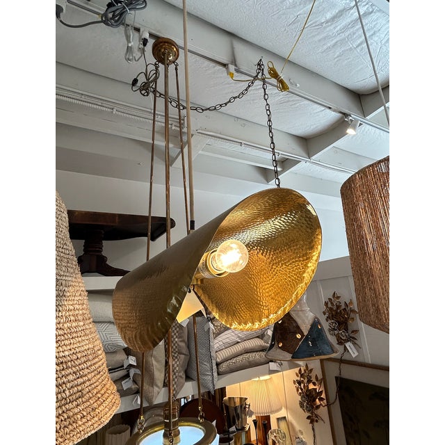 Hammered brass pendant with elongated curved shade and suspended cord support. The exterior and interior surfaces feature...