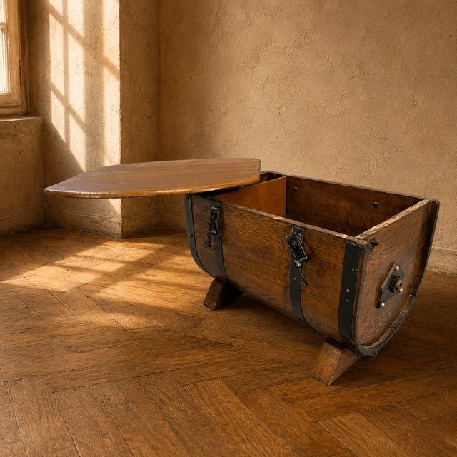A vintage oak storage chest from the 1930s–1940s, featuring a distinctive barrel-form silhouette with black metal straps...