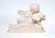 A finely carved marble sculpture depicting a reclining putto engaged in play with a serpent coiled around its arms,...