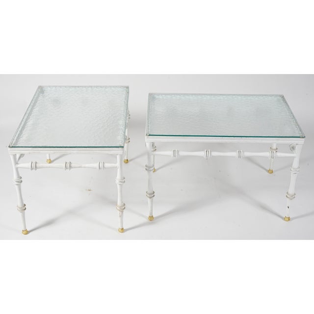 These are a pair of vintage faux bamboo tables featuring a white painted finish, gilded brass feet, and textured glass...