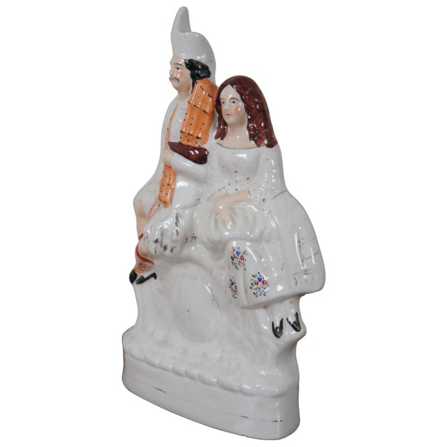 Antique circa 1870s Staffordshire porcelain figurine in the shape of a man and woman in Scottish clothing seated above a...