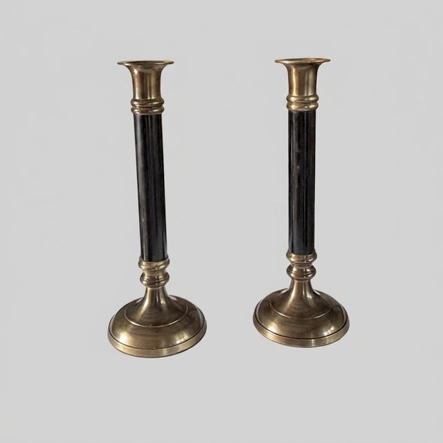 A pair of vintage candlesticks featuring slender black fluted columns with warm brass-toned mounts and broad circular...