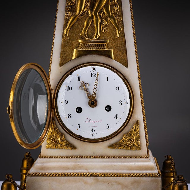 Obelisk-shaped marble clock with fire-gilt bronze appliqués, relief scene, and a surmounting armillary sphere. The clock...