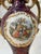 Showcasing a deep burgundy/maroon glazed porcelain body, ornate dual gold handles, and an oval central cameo medallion...
