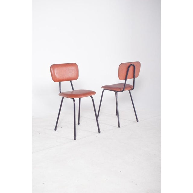 Pair of chairs in red synthetic leather. with a black tubular metal frame and upholstered seat and back, typical of 20th...