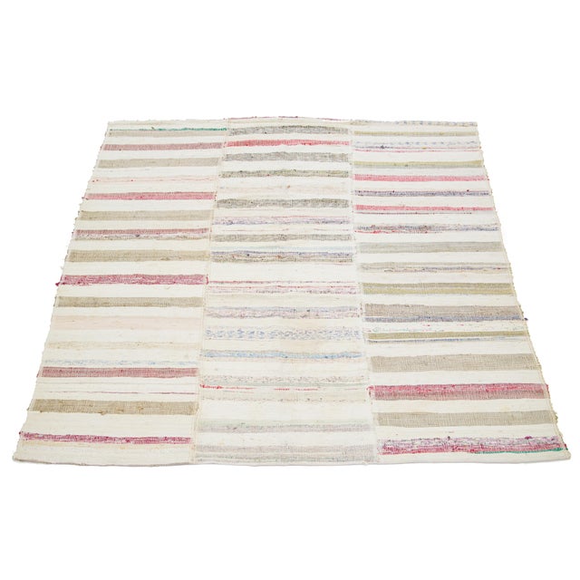 This hand-knotted Kilim wool rug has a beige field in an all-over striped design with multicolor accents. This rug...