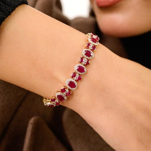 This statement tennis bracelet features oval cut natural rubies totaling 12.57 carats, set in solid 14K yellow gold....