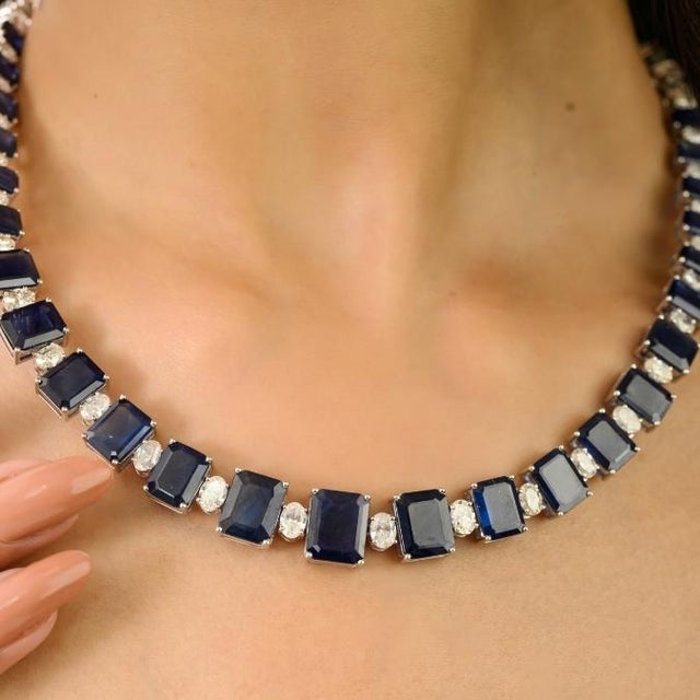 This elegant tennis necklace showcases 25 emerald cut natural blue sapphires totaling 47.64 carats, beautifully set in 18k...