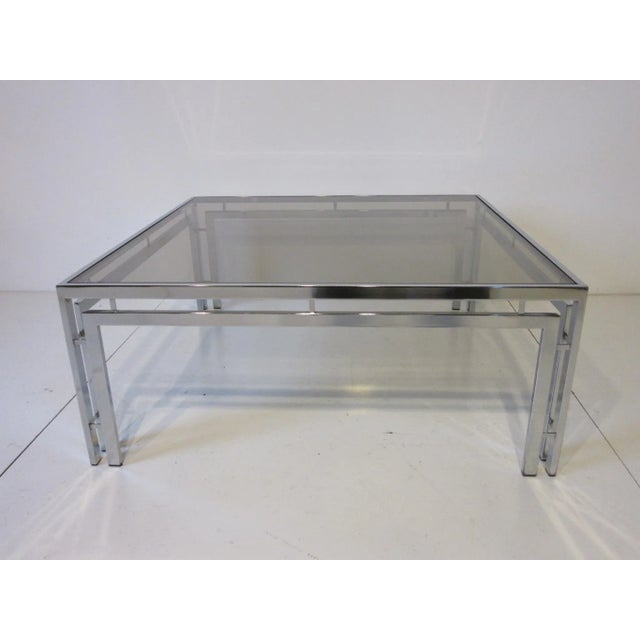 A chromed 1970's framed coffee table with a medium smoked glass top having dual frame support design details in the manner...
