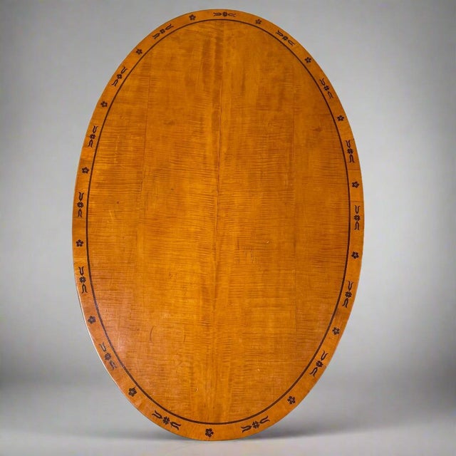 A fine Biedermeier oval library table. Ash with mahogany inlay and carved details on the base.