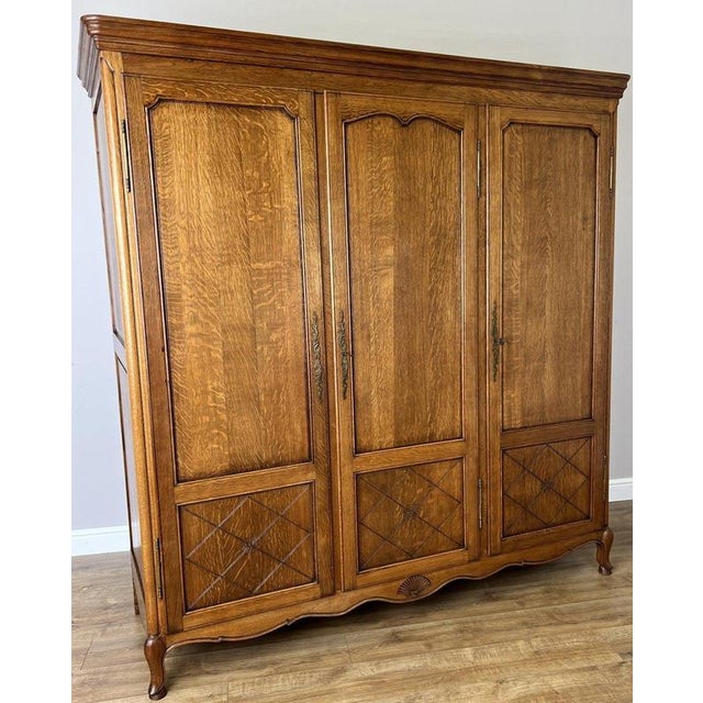 An elegant Vintage French Louis wardrobe in Oak, featuring three tall panelled doors, a warm finish with prominent grain,...