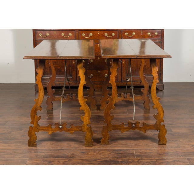 A pair of Spanish Baroque style walnut console tables from the late 19th century, with carved legs and iron stretchers....