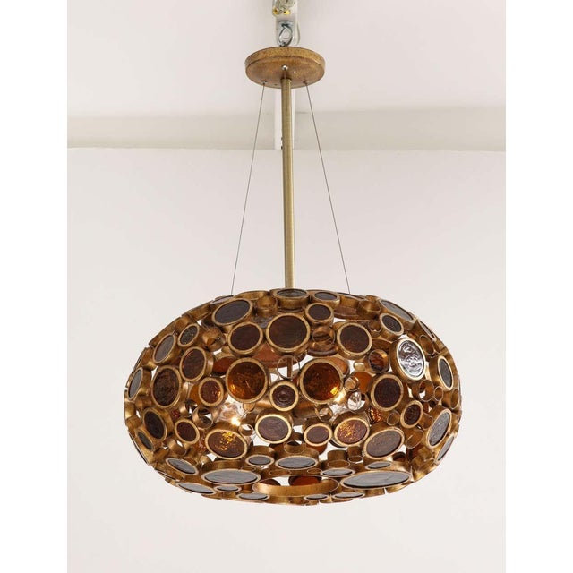 Striking sculptural pendant light featuring a brass framework inset with circular amber and smoke-toned glass lenses. The...