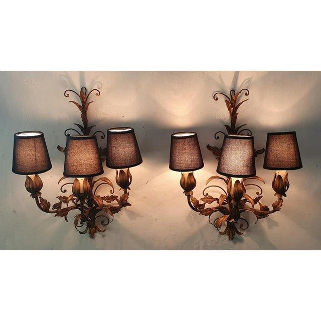 A pair of midcentury Venetian tole wall sconces, each with three lights each and decorated with gilded leaves. The candles...