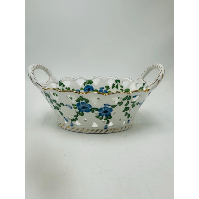 This is a decorative pierced porcelain basket dish. Appearance • Oval, shallow basket shape with two loop handles on each...