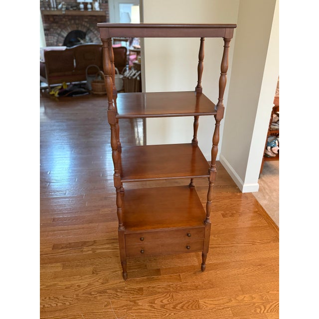 A tall four-tier wooden étagère featuring turned bobbin supports, square shelves, and a base cabinet with two small...