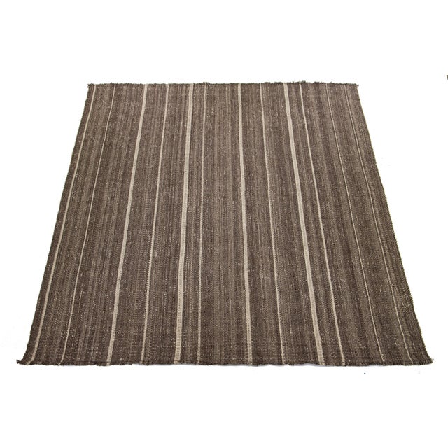 This rug features an organic, modern wool Kilim flatweave with a striped beige design and a brown base pattern. This rug...