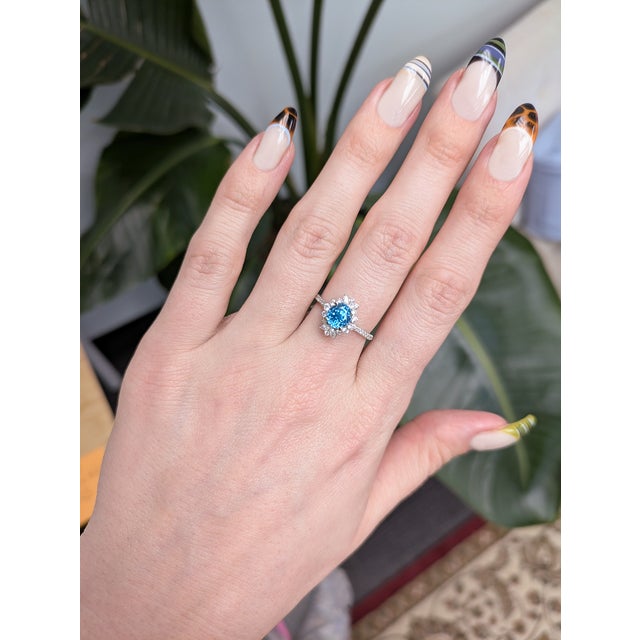 This ring features a dazzling 2.1 ct oval blue zircon measuring 6.6 × 6 mm, glowing with vivid brilliance at the center. A...