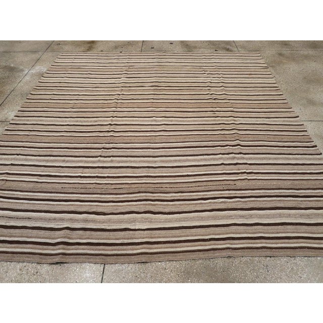 This Mid-20th century Turkish Flatweave Kilim rug, features a classic horizontal striped design, skillfully woven in a...