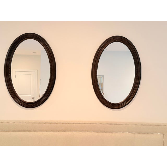 Elegant vintage pair of oval wall mirrors featuring richly finished dark wood frames with classic beaded detailing. Their...