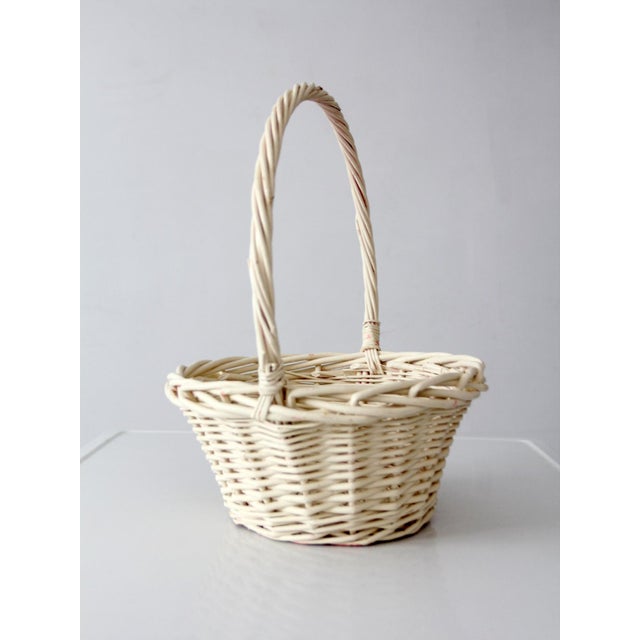 Vintage painted wicker gathering basket in a soft white finish, with an open weave and arched handle. The proportions...