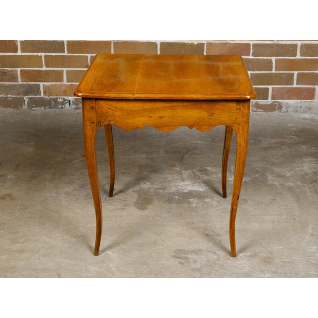 A French Louis XV style walnut side table from the early 19th century with single drawer and scalloped apron on all sides....