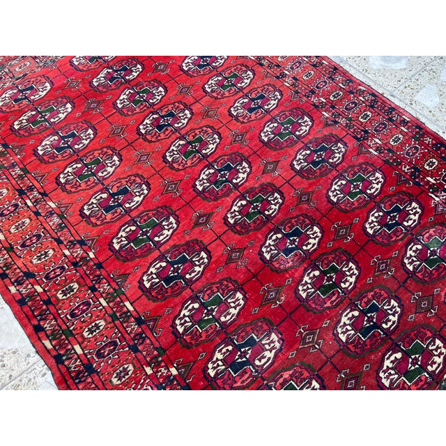 This classic Turkmen Bokhara rug showcases an allover field of repeating octagonal "gul" medallions in deep burgundy,...