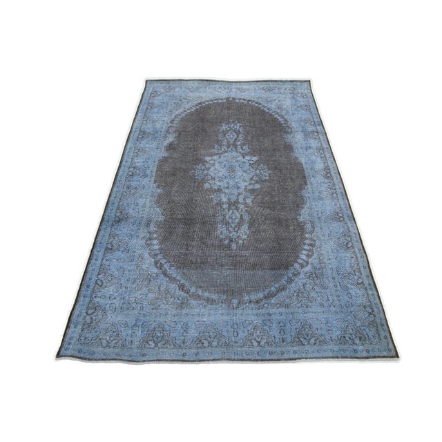 This vintage overdyed Persian wool rug features a captivating blue field with charming gray floral accents. This rug...