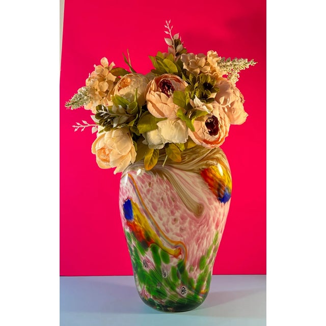 This narrow oval shaped art glass vase was hand blown by glass artisans using an array of colored glass, patterns and...