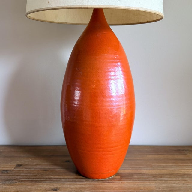 A sculptural 1960s ceramic table lamp in the manner of Jacques and Dani Ruelland, with a vivid orange glaze and...
