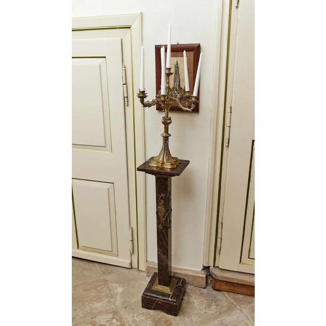 An elegant pair of decorative pedestals made of red marble with a distinctive pattern. Each column is decorated with brass...