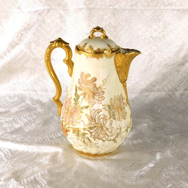 This is a cream color chocolate pot or teapot with a matte finish and what I believe to be hand painted flowers trimmed in...