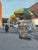 This oil on wood panel captures a vibrant street scene featuring a food vendor's cart adorned with a bright yellow and...