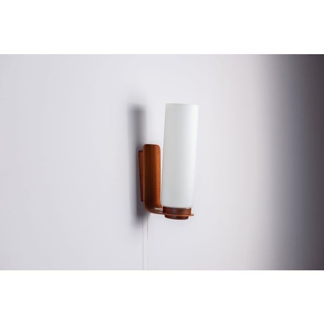 This Danish mid-century wall lamp embodies the timeless elegance of Scandinavian design. A softly glowing opal glass shade...