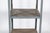 A tall, narrow industrial-style etagere with a durable gray painted metal frame and six, reclaimed weathered wood plank...